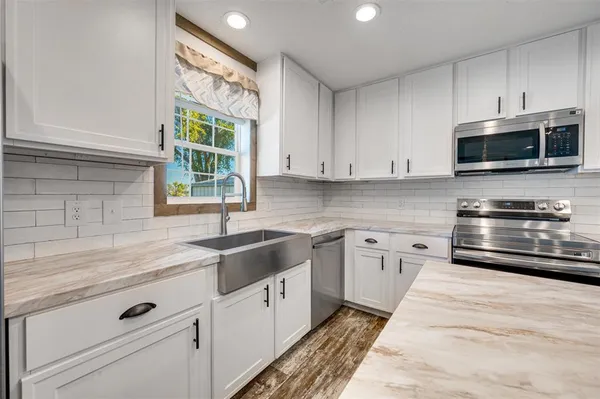 a kitchen with granite countertop white cabinets stainless steel appliances and a window