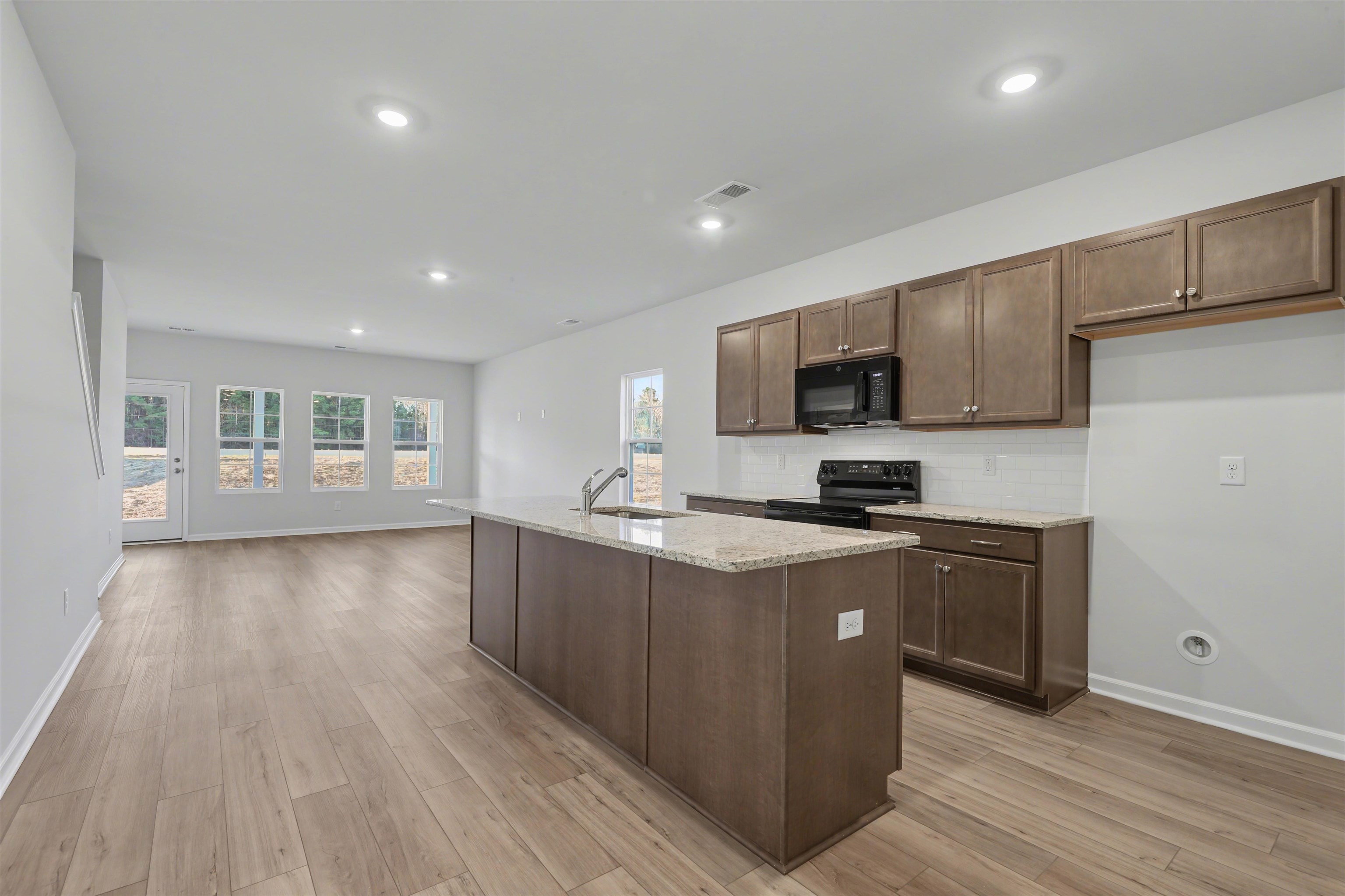 3431 Logan Street Conway, SC 29526 - Photo 8 of 31 Kitchen with light stone counters, black appliances, an island with sink, tasteful backsplash, and light wood finished floors