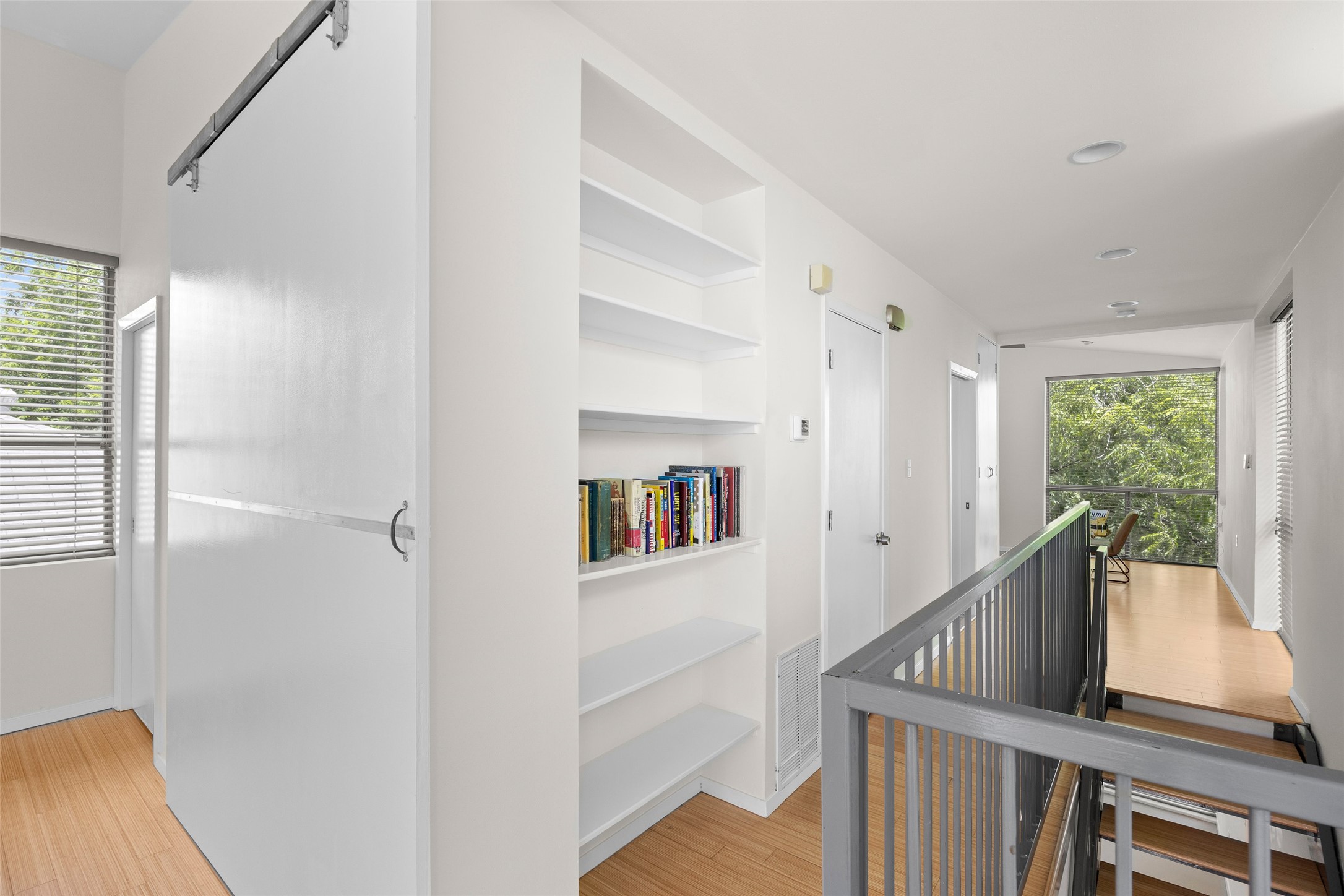 1305 Chestnut Avenue Austin, TX 78702 - Photo 23 of 40 An airy upper-level hallway features built-in shelving, hardwood flooring, and a barn door, leading to an overlook.