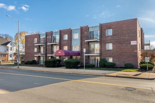 a front view of multi story residential apartment building with yard and traffic signal