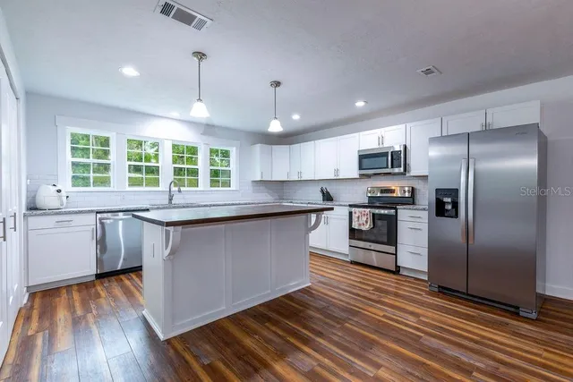 a kitchen with granite countertop a refrigerator a sink dishwasher a stove and white cabinets with wooden floor