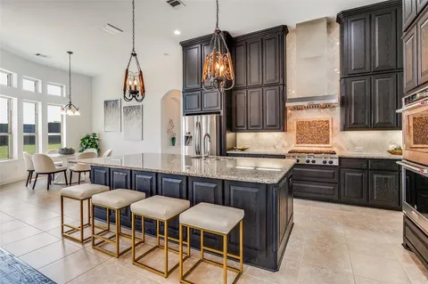 a kitchen with stainless steel appliances granite countertop a sink a stove a refrigerator and chairs