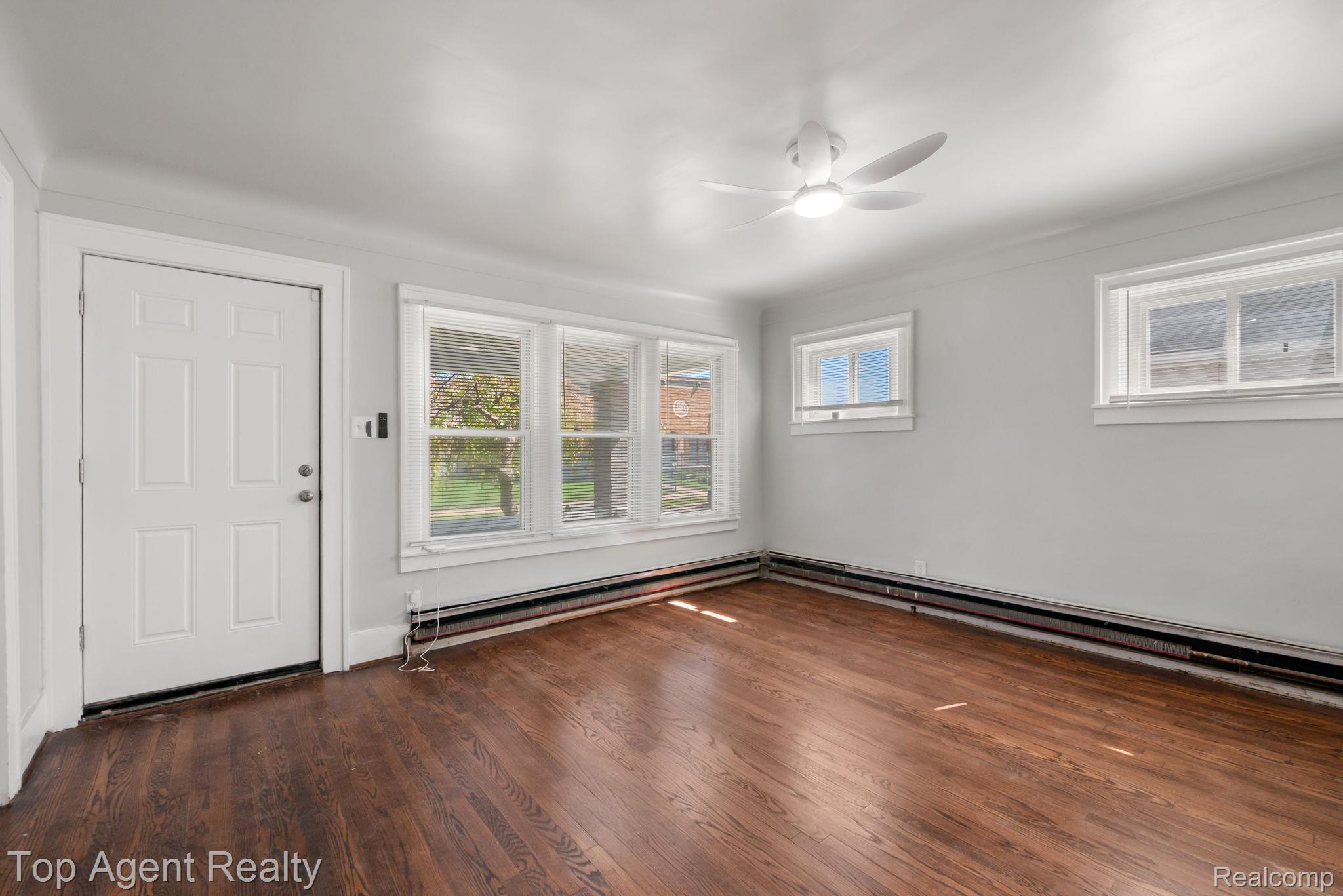 Wood-finish flooring, multiple windows, ceiling fan with integrated lighting, and a paneled entry door