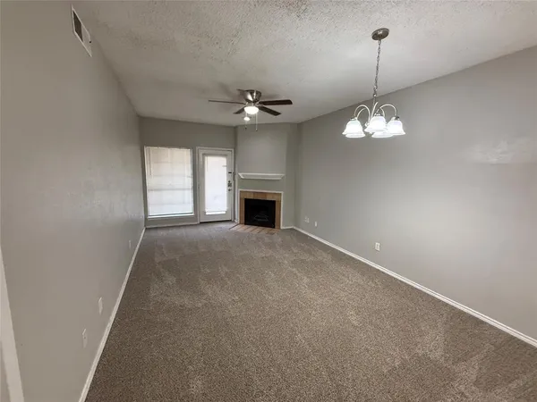 an empty room with windows fireplace and chandelier