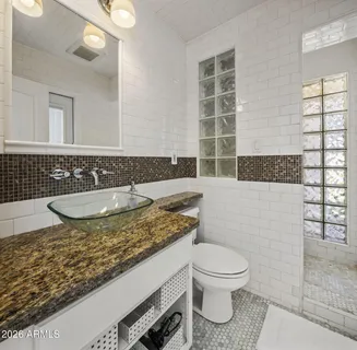 a bathroom with a granite countertop sink a toilet a mirror and shower