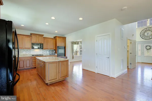 a large kitchen with stainless steel appliances granite countertop a stove a sink a refrigerator and white cabinets with wooden floor
