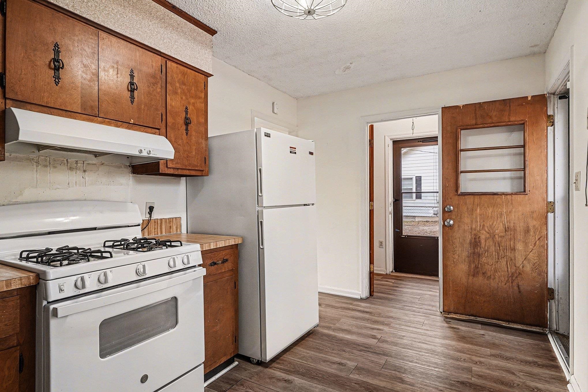 916 Brinkley Street Georgetown, SC 29440 - Photo 9 of 39 Kitchen featuring white appliances, a textured ceiling, under cabinet range hood, dark wood-style flooring, and brown cabinetry