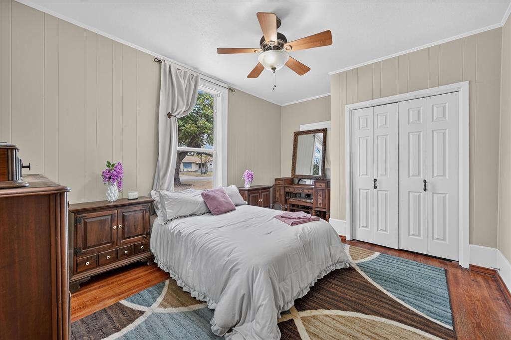 304 East Main Street Itasca, TX 76055 - Photo 25 of 38 Hardwood-style flooring, paneling wall treatment, ceiling fan with light fixture, window with drapes, and bi-fold closet doors