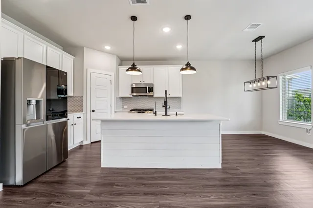 a large kitchen with stainless steel appliances kitchen island a refrigerator wooden floor and a view of living room