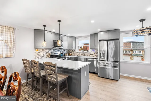 a kitchen with stainless steel appliances kitchen island granite countertop a refrigerator a stove a sink a dining table and chairs with wooden floor
