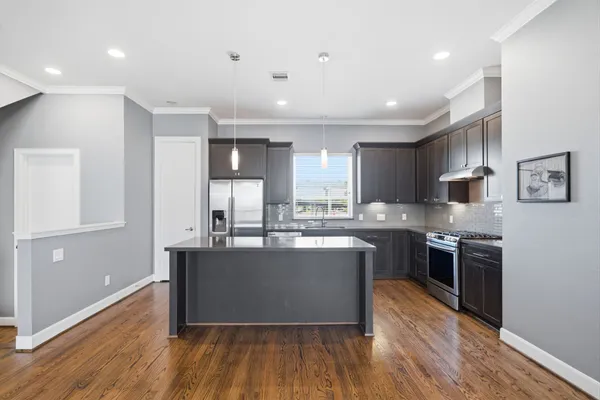 a kitchen with stainless steel appliances granite countertop a stove top oven a sink dishwasher a refrigerator and a dining table with wooden floor
