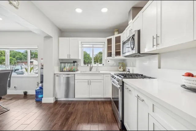 a kitchen with granite countertop a sink cabinets stainless steel appliances and a window