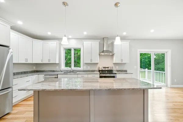 a kitchen with kitchen island granite countertop a stove a sink a refrigerator and white cabinets with wooden floor