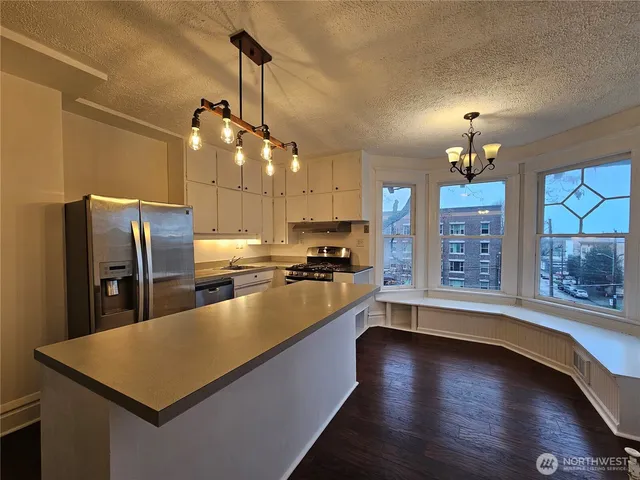 a kitchen with stainless steel appliances granite countertop a refrigerator a sink dishwasher a stove and a dining table with wooden floor