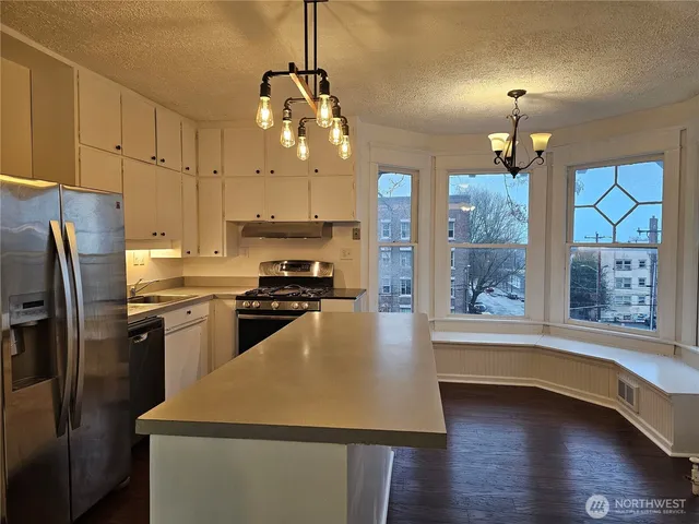 a kitchen with stainless steel appliances granite countertop a refrigerator a sink dishwasher a stove and white countertops with wooden floor