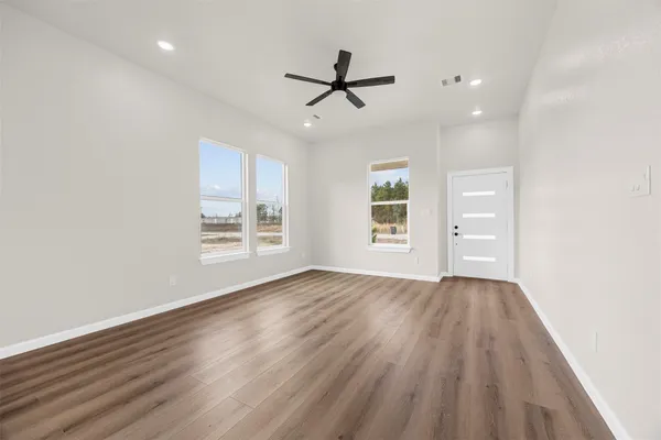 an empty room with wooden floor ceiling fan and windows