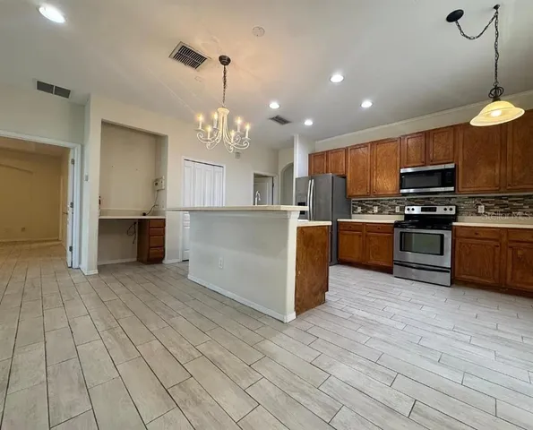 a large kitchen with stainless steel appliances granite countertop a stove top oven a sink dishwasher a refrigerator and a dining table with wooden floor