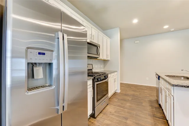 a kitchen with stainless steel appliances granite countertop a refrigerator a stove and a sink with wooden floor