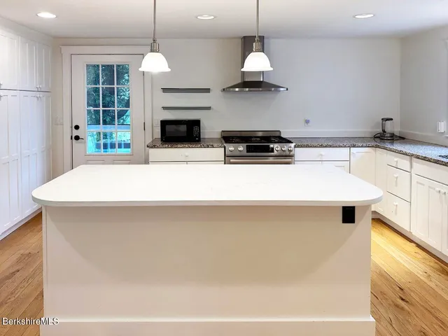 a kitchen with kitchen island granite countertop a stove a sink a center island and windows