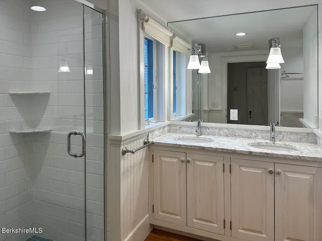 a bathroom with a granite countertop sink two mirror and shower