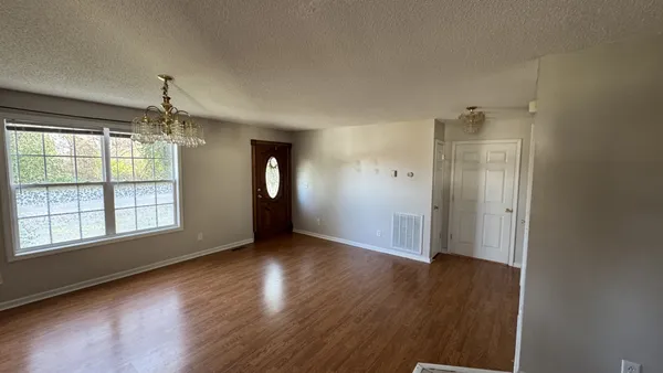 an empty room with wooden floor chandelier and windows