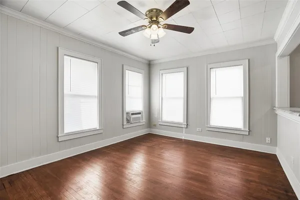 an empty room with wooden floor chandelier fan and windows