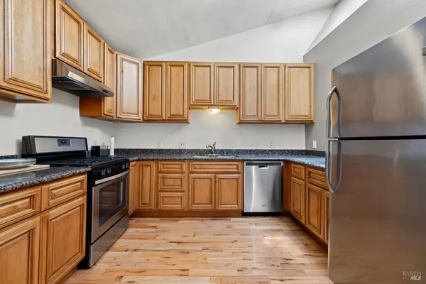 a kitchen with stainless steel appliances granite countertop a refrigerator a sink dishwasher a stove and oven with wooden floor
