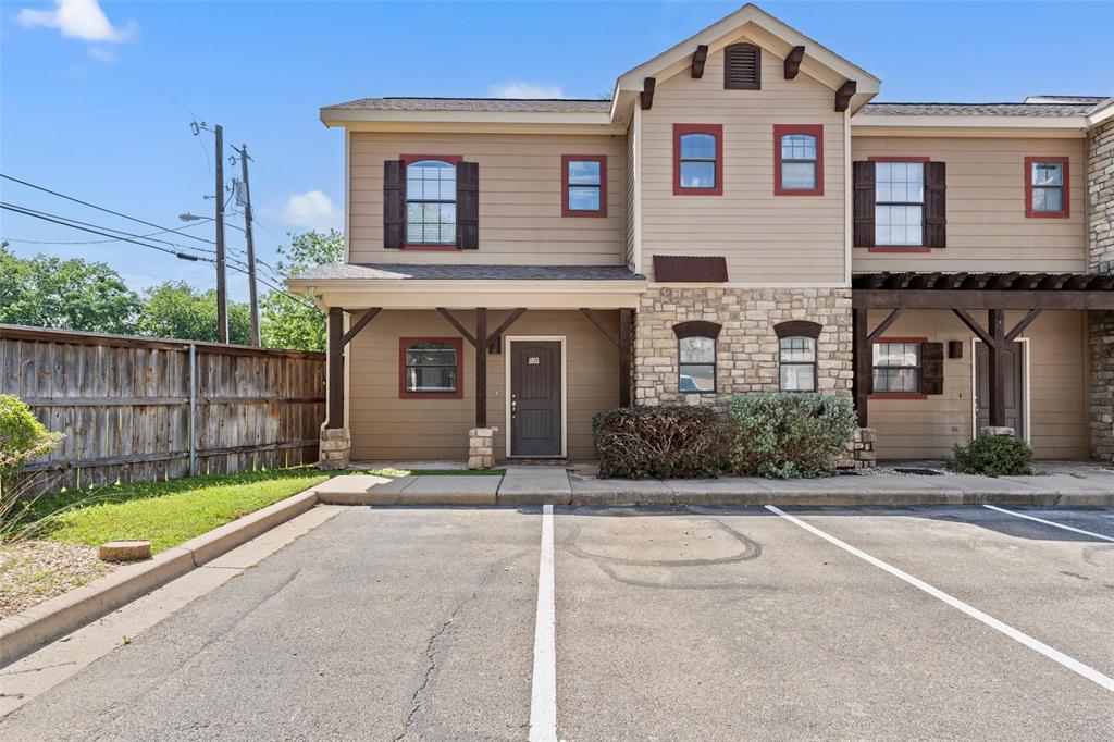 Townhome / multi-family property with uncovered parking, stone siding, and a shingled roof