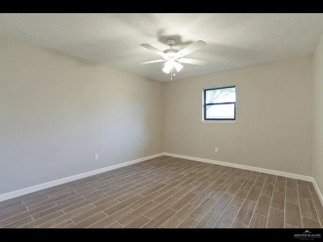 a view of an empty room with chandelier fan and wooden floor