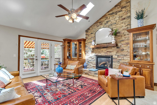 2863 Fallentine Road Sandy, UT 84093 - Photo 18 of 48 Vaulted ceiling living area featuring a stone accent wall with fireplace, wood-finish flooring, two built-in display cabinets, a ceiling fan, and French doors opening to an outdoor area
