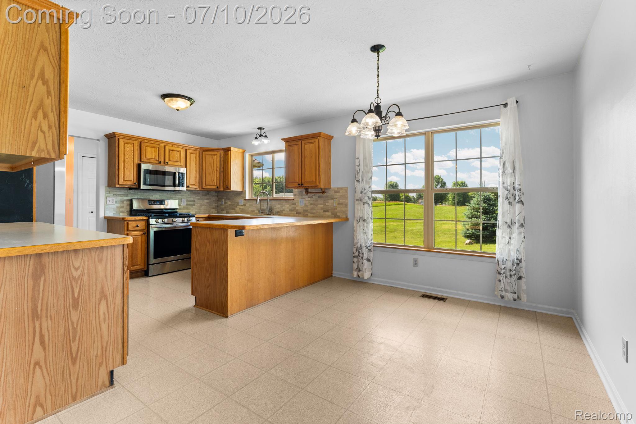 3144 North Nicholson Road Fowlerville, MI 48836 - Photo 38 of 70 Open-concept kitchen and dining area featuring wood cabinetry, stainless steel appliances, a breakfast bar, and large windows with a green landscape backdrop