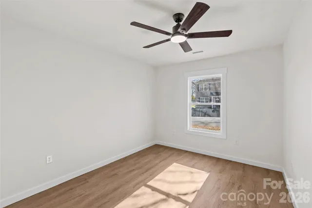 an empty room with wooden floor fan and windows