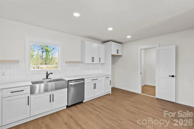 a kitchen with white cabinets a sink dishwasher and a stove with wooden floor