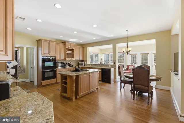 a kitchen with stainless steel appliances granite countertop a stove top oven a sink a dining table and chairs with wooden floor