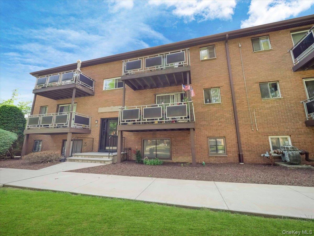 27 Tanager Road, Unit 2702 Monroe, NY 10950 - Photo 29 of 35 Multi-level brick exterior building featuring individual balconies with metal railings, a central entry door, mature shrubbery, and a well-maintained lawn
