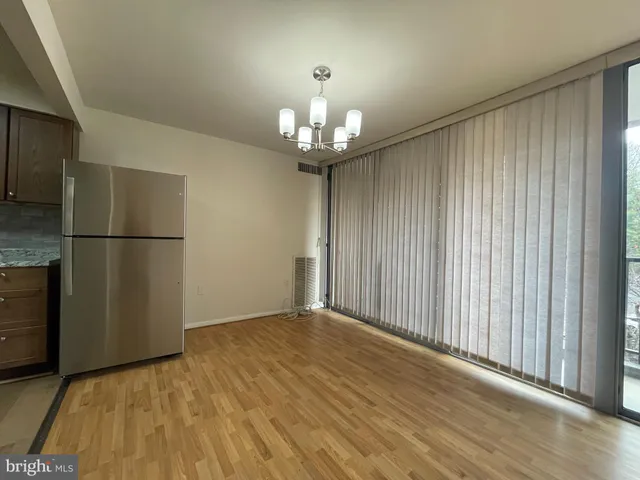 a view of an empty room with wooden floor and a kitchen