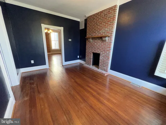 a view of an empty room with wooden floor and a fireplace