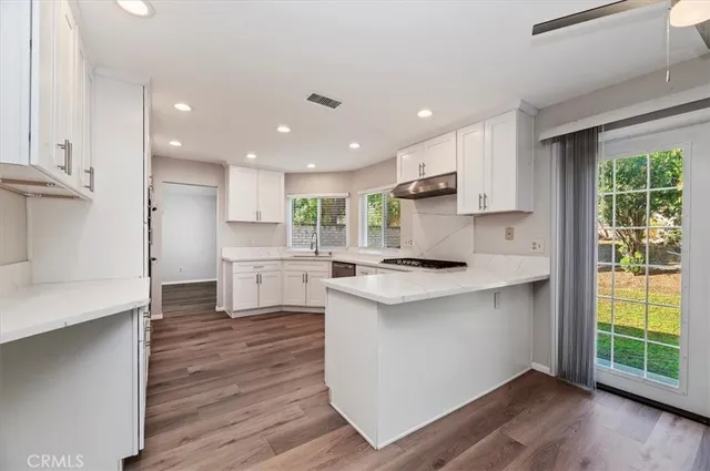 a kitchen with kitchen island wooden floors white cabinets appliances and a window