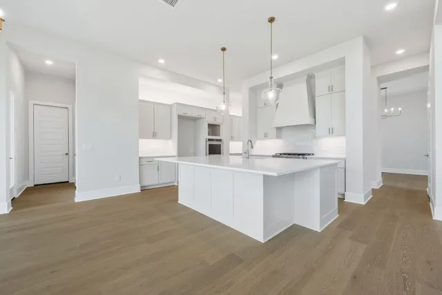 a large white kitchen with kitchen island a refrigerator a sink dishwasher a stove and a dining table with wooden floor