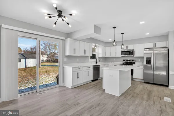 a kitchen with granite countertop a refrigerator a stove a sink and white cabinets with wooden floor