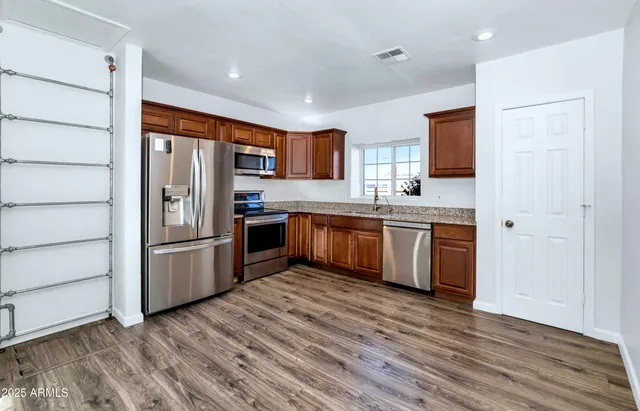 a kitchen with stainless steel appliances granite countertop a refrigerator a sink dishwasher a stove with wooden cabinets and floor