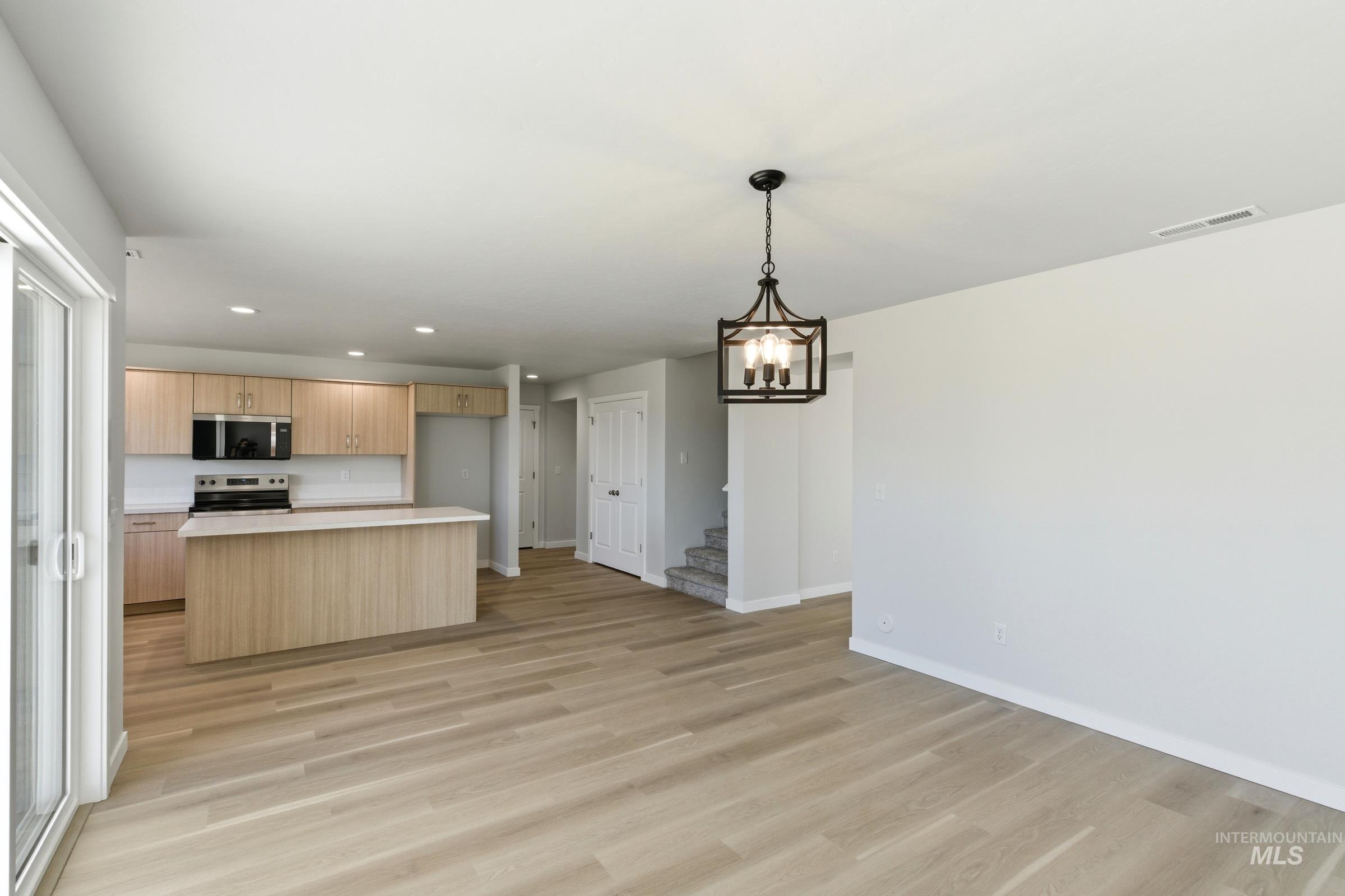 13677 Redway Court Caldwell, ID 83607 - Photo 8 of 35 Open-concept living area featuring light wood-finish flooring, a contemporary black metal chandelier, and a kitchen with light wood-finish cabinetry, a large center island with a light-toned countertop, and stainless steel appliances