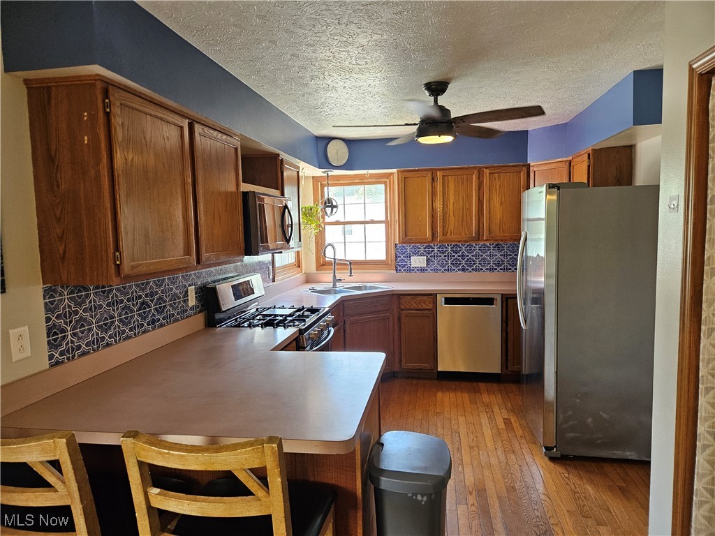 6247 Hathaway Road Cleveland, OH 44125 - Photo 13 of 42 Kitchen featuring stainless steel appliances, a peninsula, a ceiling fan, light wood-style flooring, and tasteful backsplash