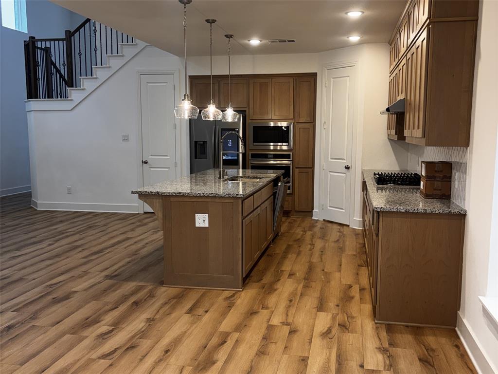 2828 Walden Road Celina, TX 75009 - Photo 4 of 30 Modern kitchen featuring stainless steel appliances, wood-finish flooring, granite countertops, a central island with sink, and pendant lighting