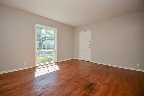 a view of an empty room with wooden floor and a window