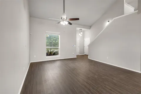 an empty room with wooden floor chandelier fan and windows