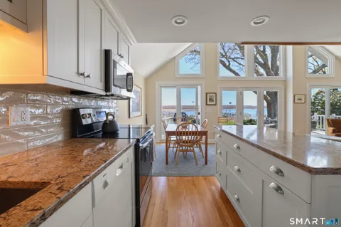 a kitchen with stainless steel appliances granite countertop a stove top oven a sink dishwasher a dining table and chairs with wooden floor