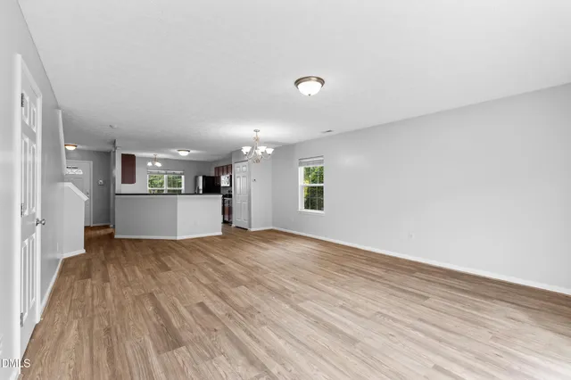 a view of empty room with wooden floor and kitchen