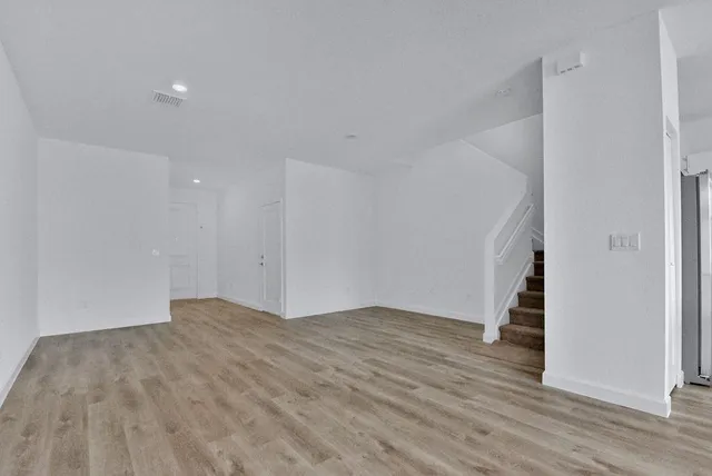 a view of an empty room with wooden floor and stairs