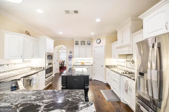 a kitchen with stainless steel appliances granite countertop a stove top oven a refrigerator a sink and white cabinets with wooden floor